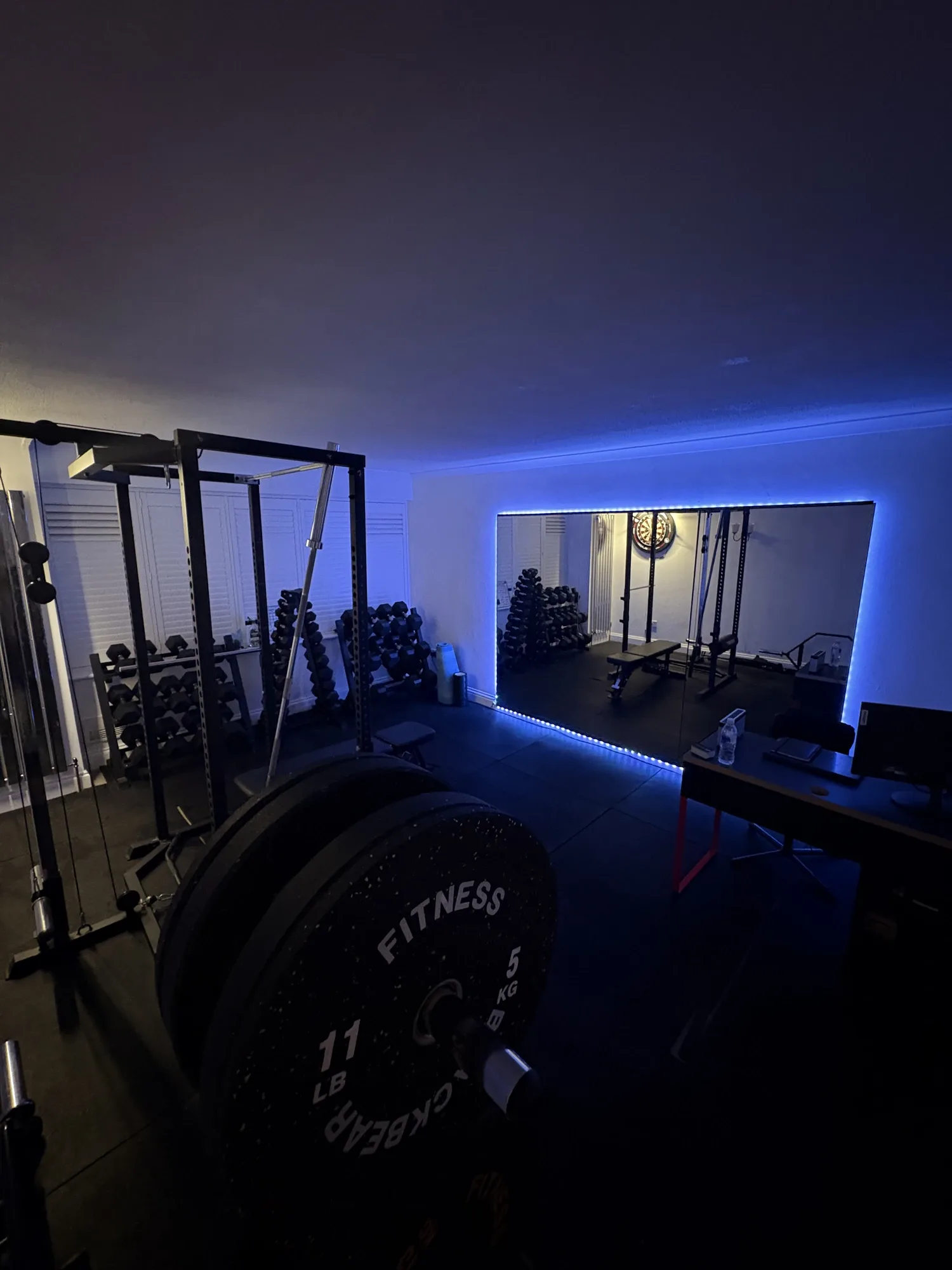 The JE Training studio after dark — LED-lit mirror, dumbbells and full rack